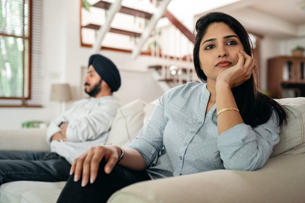 Sad young Indian woman avoiding talking to husband while sitting on sofa, real estate investment, India, property investment, pros and cons, REITs, Real estate investment in India